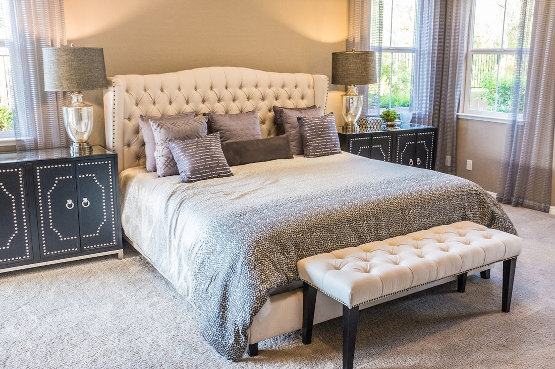 A tufted headboard bed with grey patterned bedding and a cream bench in a bedroom