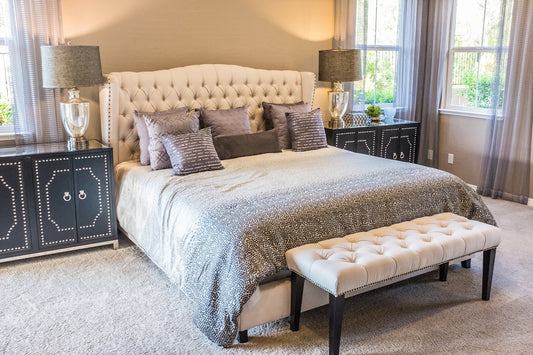 A tufted headboard bed with grey patterned bedding and a cream bench in a bedroom