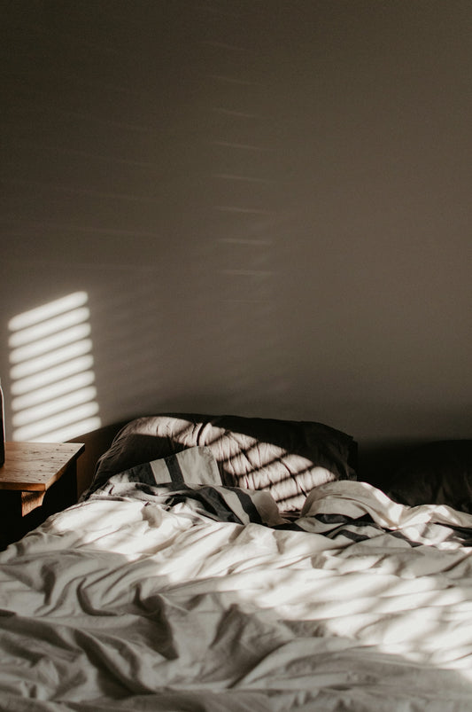 A rumpled bed with striped bedding in a room with slatted light patterns