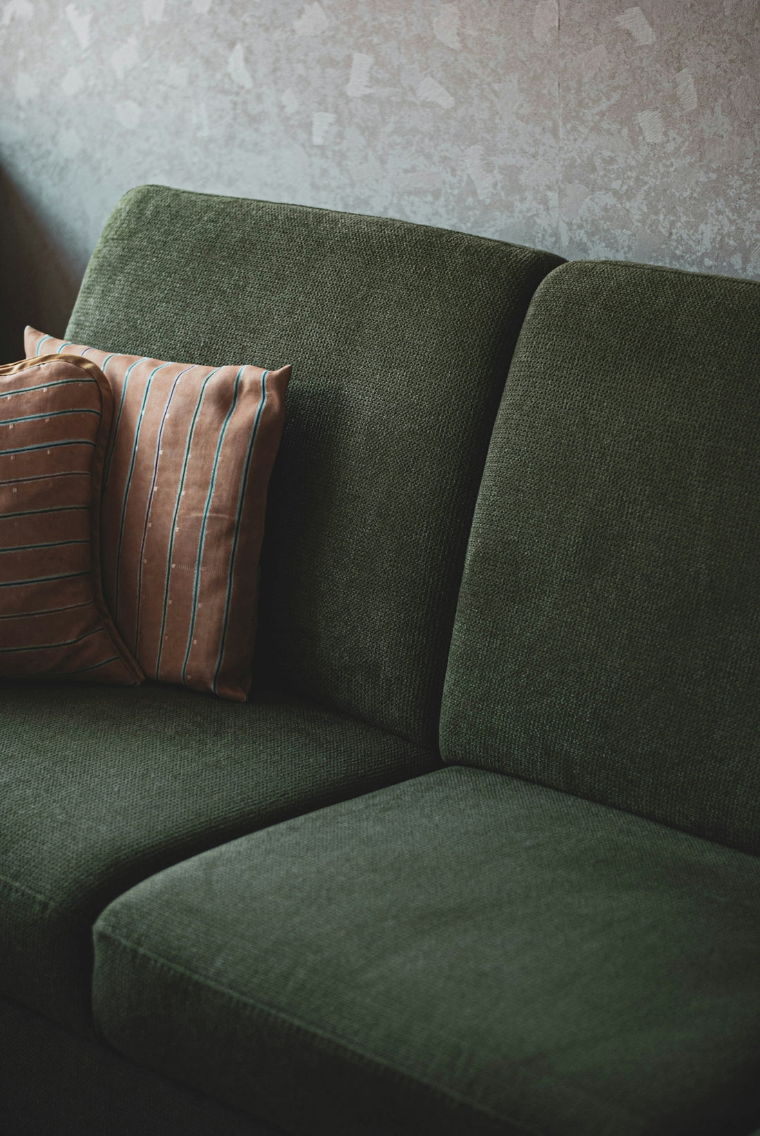 A dark green textured sofa with two striped cushions against a neutral wall