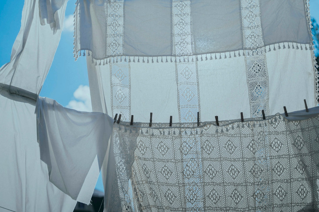 White lace curtains hanging on a clothesline against a bright blue sky