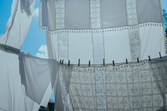 White lace curtains hanging on a clothesline against a bright blue sky